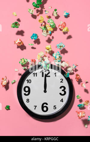 Il popcorn di differenti colori che ricadono su un orologio a dodici contro un sfondo rosa Foto Stock