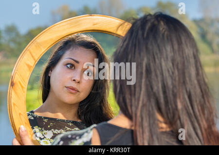 Giovane donna guardando l'immagine speculare in natura Foto Stock