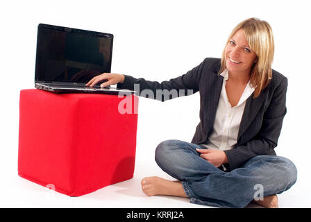 Junge Geschaeftsfrau sitzt neben Laptop, der auf einem roten Stoffwuerfel steht - young business donna accanto al laptop Foto Stock