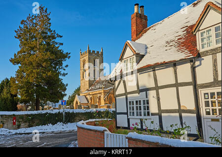 La chiesa di San Pietro, Welford on Avon, e per metà in legno bianco e nero cottage su un inverno mattina con cielo blu dopo una leggera nevicata. Foto Stock