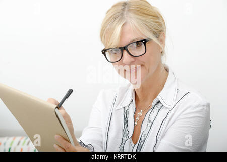 Bella donna matura la scrittura su un notebook Foto Stock