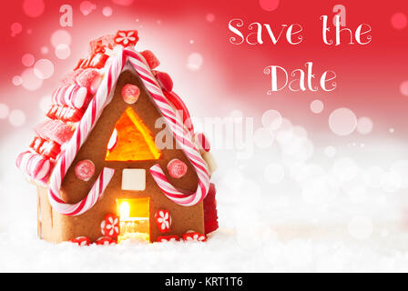 Testo inglese per salvare la data. Gingerbread House di scenario innevato come decorazione di Natale. Lume di candela per atmosfera romantica. Sfondo rosso con effetto Bokeh di fondo. Foto Stock