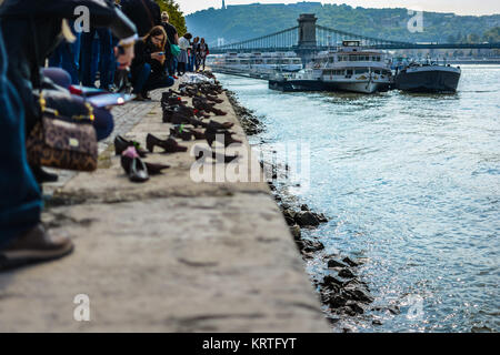 Le scarpe sulla sponda del Danubio, un memoriale a Budapest, in Ungheria con il Ponte delle catene e delle barche in background come turisti scattare foto Foto Stock