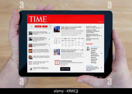 Un uomo guarda la rivista Time sito web sul suo iPad dispositivo tablet, sparato contro un tavolo di legno top sfondo (solo uso editoriale) Foto Stock