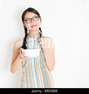 Ragazza orientale di mangiare con bacchette e pensare Foto Stock