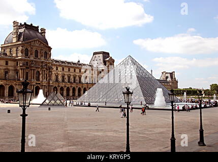 Vista del cortile principale del Palazzo del Louvre e con il vetro e metallo Piramide (Pyramide du Louvre), e numerosi turisti che si godono la giornata di sole Foto Stock