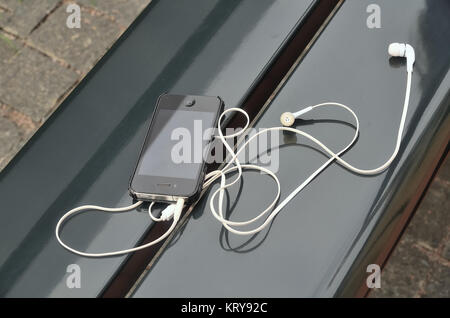 Il telefono nero con cuffie bianche si trova sul banco di strada Foto Stock