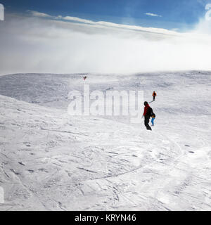 Gli sciatori e gli snowboarder in discesa su pendio nevoso e il cielo con la luce del sole di nuvole a sun giorno d'inverno. Montagne del Caucaso, Georgia, regione Gudauri. Foto Stock