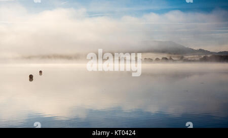 La nebbia si alza dalle tranquille acque del lago di Windermere a Ambleside in Inghilterra del Parco Nazionale del Distretto dei Laghi. Foto Stock