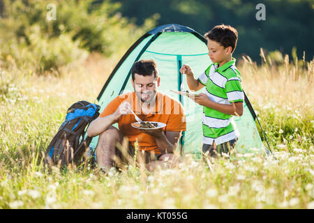 Padre e figlio sono in campeggio in natura. Essi stanno mangiando. Foto Stock