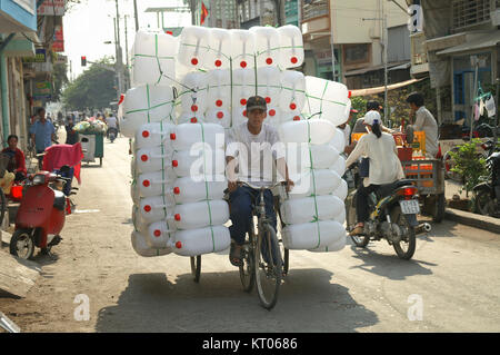 CHAU DOC, VIETNAM - 30 gennaio 2005 : un uomo di trasportare un gran numero di vuoti in materiale plastico taniche strapped precariamente ai suoi tre ruota bicicletta. Foto Stock