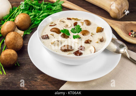 Una foto di una piastra di un fungo minestra in crema con champignon, cremini, prezzemolo fresco e pepe, al buio su un rustico texture di sfondo con un posto per Foto Stock