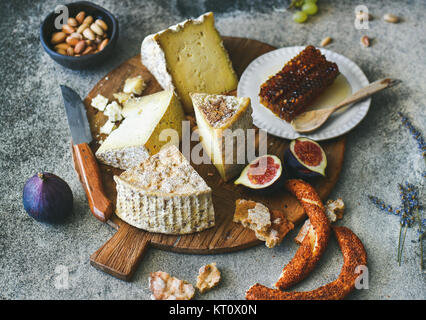 Un vassoio di formaggi con assortimento di formaggi, fichi, miele, pane appena sfornato e i dadi sul pannello di legno su cemento grigio Sfondo. Parte o per la raccolta di mangiare Foto Stock