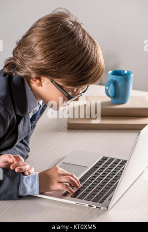 Schoolchild in business suit utilizzando il computer portatile Foto Stock