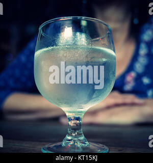 Bicchiere di vino su una tabella con la donna seduta dietro Foto Stock