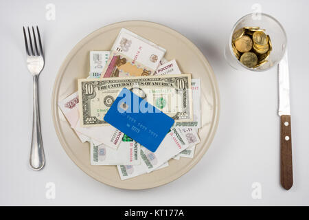 Sulla piastra è un sacco di soldi e una plastica carta di credito, in piedi accanto a un bicchiere e una forchetta e coltello giacciono, vista dall'alto Foto Stock