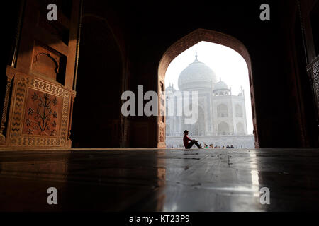 Western donna seduta sotto un arco al Taj Mahal con il mausoleo nel retro, Agra,Uttar Pradesh, India. Foto Stock