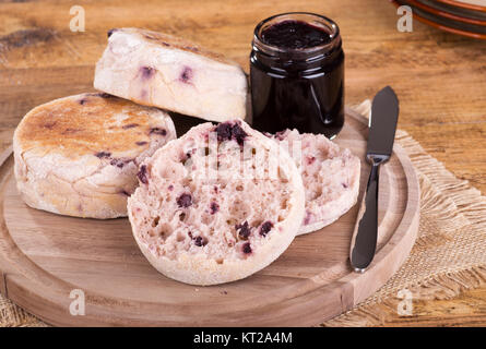 Mirtillo muffin inglesi su un tagliere di legno con un vasetto di marmellata Foto Stock