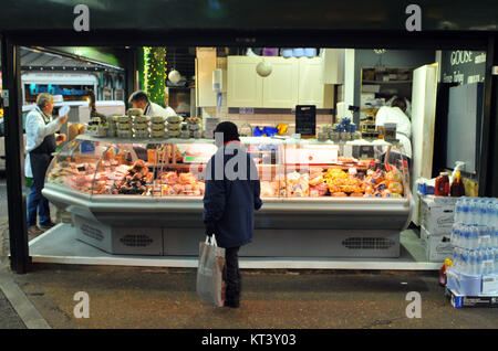Una donna che guarda le varie carni in vendita su un mercato di macellai stallo a Borough Market a Southwark, Londra. Tipi diversi di carne visualizzati in corrispondenza di una macelleria Foto Stock