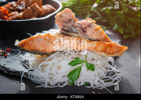 Cellophane con pezzi di salmone arrosto con i pomodori, la cipolla e il prezzemolo nel Consiglio di Amministrazione di nero ardesia Foto Stock
