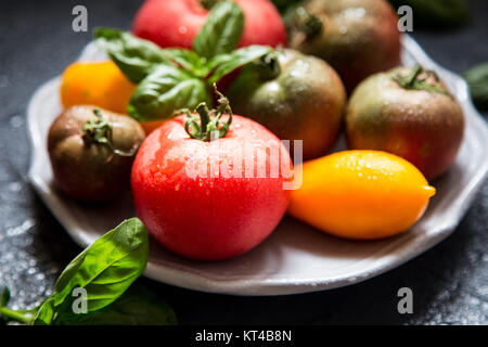 Pomodori colorati di varie dimensioni e tipologie con basilico. messa a fuoco selettiva. Foto Stock