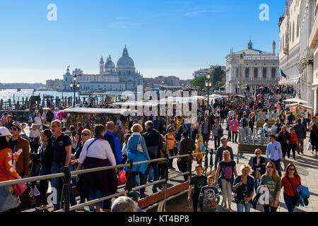 I turisti al waterfront promenade Riva degli Schiavoni vicino a San Marco con Santa Maria della Salute in background, Venezia, Italia Foto Stock