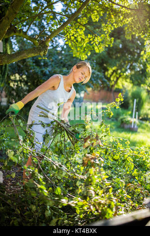 Piuttosto, giovane donna giardinaggio nel suo giardino, il taglio di rami, preparare il frutteto per l'inverno Foto Stock