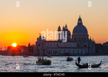 Colorato arancione tramonto sulla laguna di Venezia e la Basilica di Santa Maria della Salute con barche e una gondola con i turisti in primo piano Foto Stock