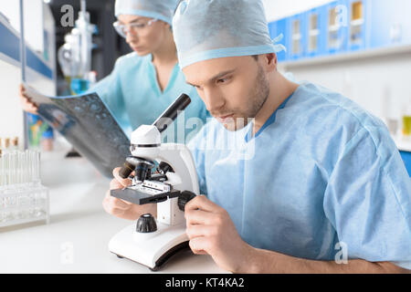 Vista laterale del chirurgo guardando attraverso il microscopio e medico analisi di immagine a raggi x Foto Stock