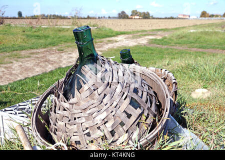 Vecchio vetro demijohn avvolto in vimini abbandonato Foto Stock