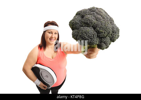 Il sovrappeso donna con una bilancia e broccoli isolati su sfondo bianco Foto Stock