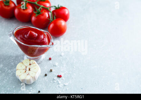 Tomato Ketchup Salsa con aglio, le spezie e le erbe aromatiche con pomodorini in una ciotola di vetro sul tavolo di pietra, il fuoco selettivo Foto Stock