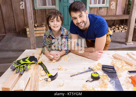 Felice padre e figlio appoggiata sul tavolo con gli attrezzi e sorridente in telecamera Foto Stock