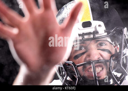 Vista da vicino aggressivo uomo nel casco riproduzione di football americano su nero Foto Stock