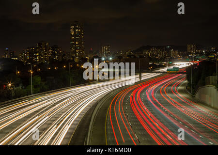 Sentieri di luce di veicoli in Kapiolani uscita per l'autostrada guardando verso le luci di Waikiki di Oahu, Hawaii lungo un avvolgimento multi-lane motorway Foto Stock