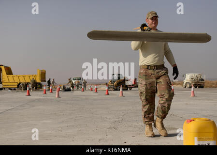 Il personale Sgt. Joshua Swertfager, nativo di Fresno, California, assegnato per la 332Expeditionary ingegnere civile Squadron porta una spatola di grandi dimensioni in un altro luogo dopo la levigatura fuori da un recente versata soletta di calcestruzzo sulla pista di una località segreta nel sud-ovest Asia nov. 28, 2017. Swertfager, una apparecchiatura pesante operatore ha lavorato con altri membri squadrone per la riparazione di una pista a causa di usura e rottura di uso costante da parte degli Stati Uniti e le forze della coalizione hanno battenti sortite contro ISIS. (U.S. Air Force Foto Stock