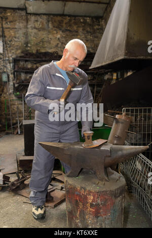 Senior fabbro maschio utilizzando un martello su incudine Foto Stock