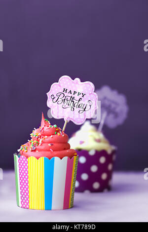 La fragola e vaniglia tortine con piccoli cuori decorativi e buon compleanno segno, contro lo sfondo viola; sullo sfondo di partito Foto Stock