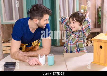 Felice padre e figlio facendo birdhouse e guardando ogni altro in officina Foto Stock