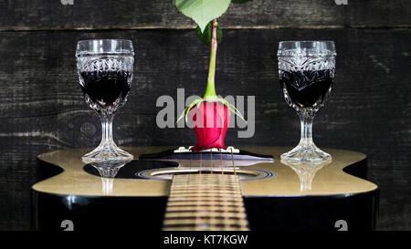 Red Rose e bicchieri di vino in appoggio su una chitarra acustica con sfondo di legno Foto Stock