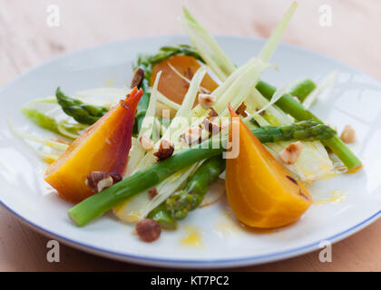 Golden barbabietole con asparagi verdi con sedano rapa e rasata, frantumato di nocciole, il succo di limone medicazione sulla piastra bianca sul tavolo di legno Foto Stock