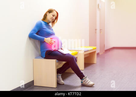 Gravidanza caucasico giovane donna seduta in sala di attesa e di sofferenza forti dolori addominali. Foto Stock