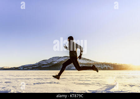 In inverno in esecuzione nella neve runner maschio sullo sfondo di montagne e di sun Foto Stock