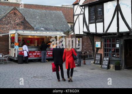 I clienti acquistano street food & persone con borse per lo shopping a piedi attraverso il caos del mercato, un mercato storico area in York - North Yorkshire, Inghilterra, Regno Unito. Foto Stock