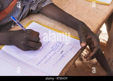 Un capretto a lavorare a scuola in Burkina Faso. Primo piano sulla sua cartella di lavoro mentre si sta scrivendo una lezione. Immagine circa l'istruzione in Africa. Foto Stock