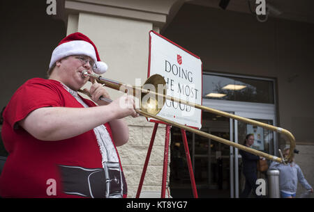 Wesley Chapel, FL, Stati Uniti d'America. 22 Dic, 2017. Un giovane Esercito della Salvezza volontario in una Santa shirt svolge il suo trombone accanto alla sua 'Rosso bollitore" al di fuori di un pubblico fruttivendolo, raccogliere donazioni per l'organizzazione. Credito: Robin Rayne Nelson/ZUMA filo/Alamy Live News Foto Stock