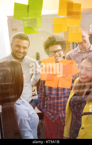 I giovani creativi startup business persone sulla riunione in ufficio moderno facendo piani e progetti con gli adesivi di post su vetro Foto Stock