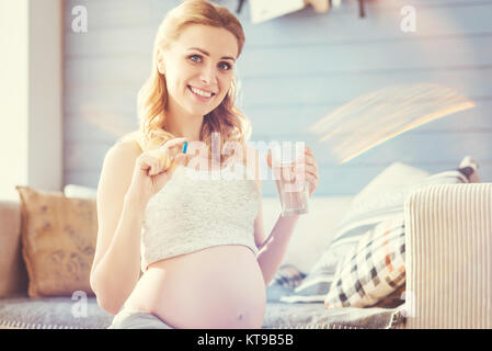 Prendersi cura della propria salute. Positivo bella donna incinta di prendere pillole e appoggiata a casa mentre vi godete il congedo di maternità Foto Stock