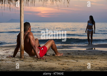 Luna di Miele romantica giovane in amore permanente sulla spiaggia su arancione tramonto sfondo, felice coppia giovane holding hands godendo oceano sunrise durante il tempo tr Foto Stock