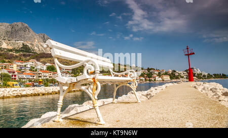 Banca bianco su una banchina del mediterraneo con una città in background Foto Stock